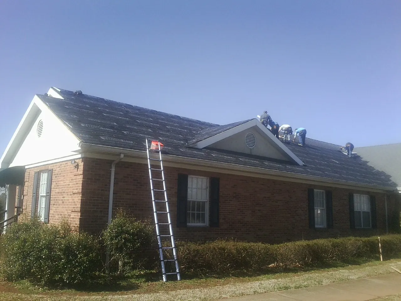 Crew tearing shingles off a brick ranch roof with a ladder set — Metal Roof Repair work by our crew in East Rutherford