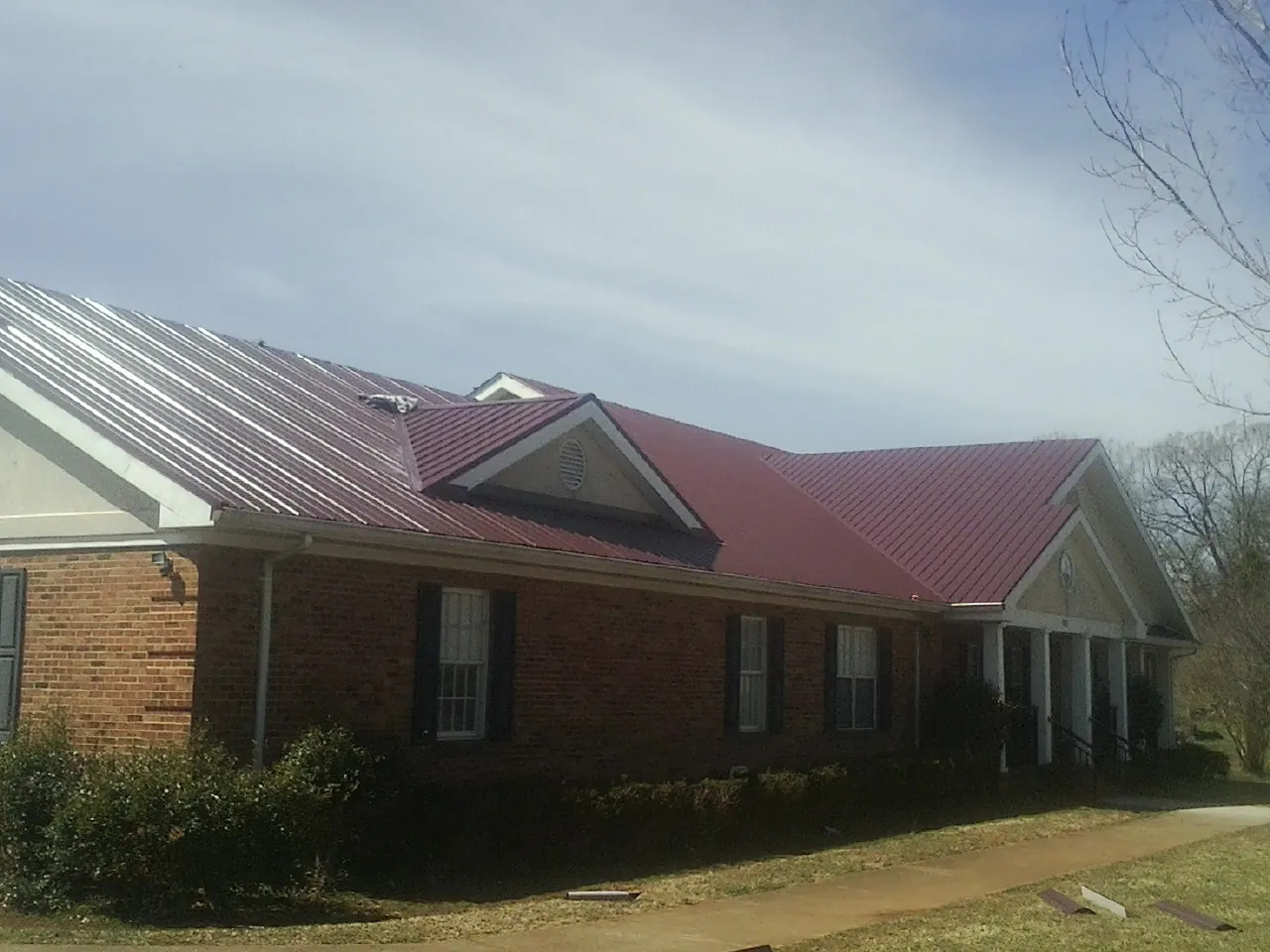 Red metal roof with gabled entries on a long brick building, from a Hail Damage Roof Repair job in East Rutherford