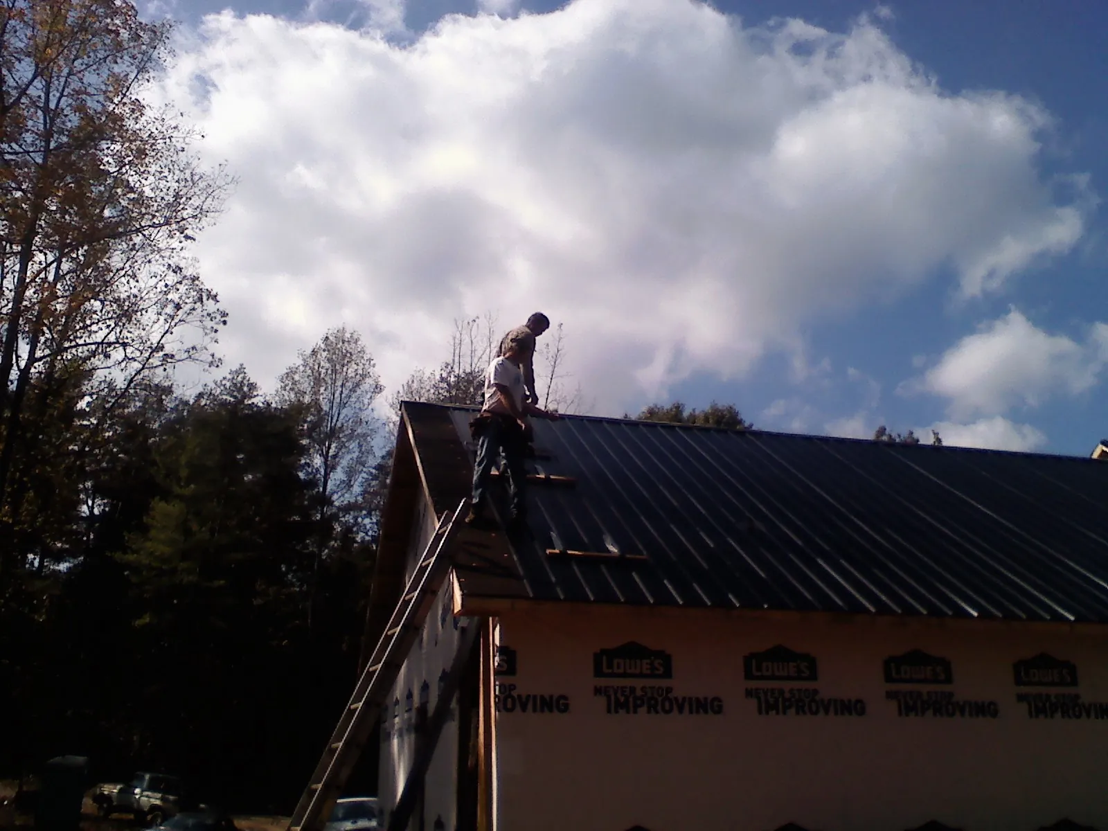 Roofer fastening dark metal panels high against a cloudy sky, from a Roof Inspection job in East Rutherford