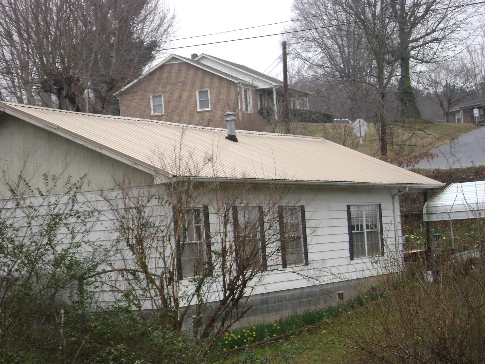 Tan metal roof on a white sided house set into a hillside — Commercial Roofing by Roofing Brothers in East Rutherford